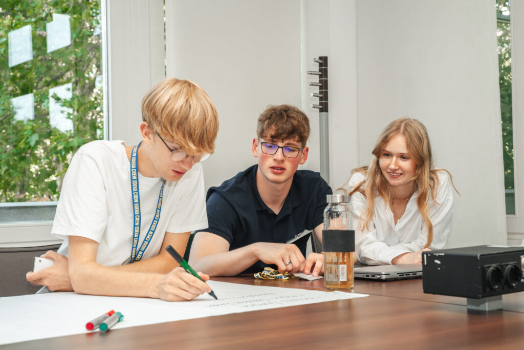Drei IT Auszubildende sitzen am Tisch und sprechen über ein Projekt