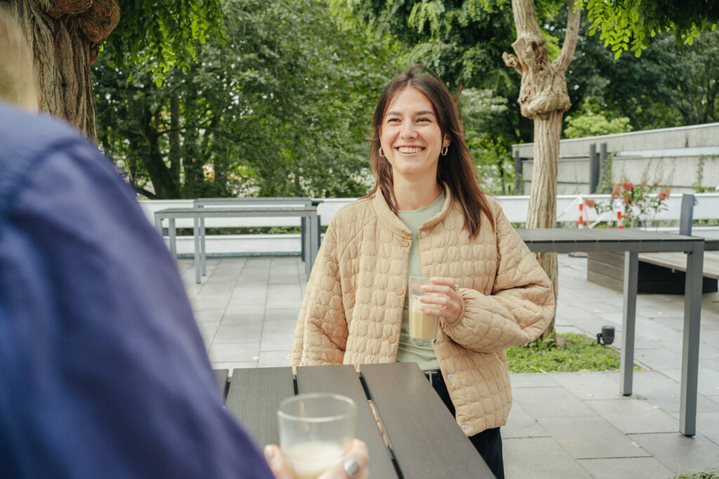 Eine IT Werkstudierende hält einen Kaffeebecher in der Hand und lächelt in die Kamera