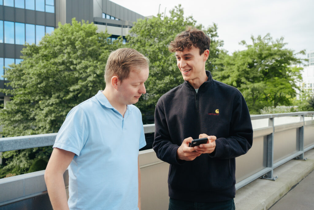 Zwei IT Kollegen unterhalten sich und schauen dabei auf ein Smartphone